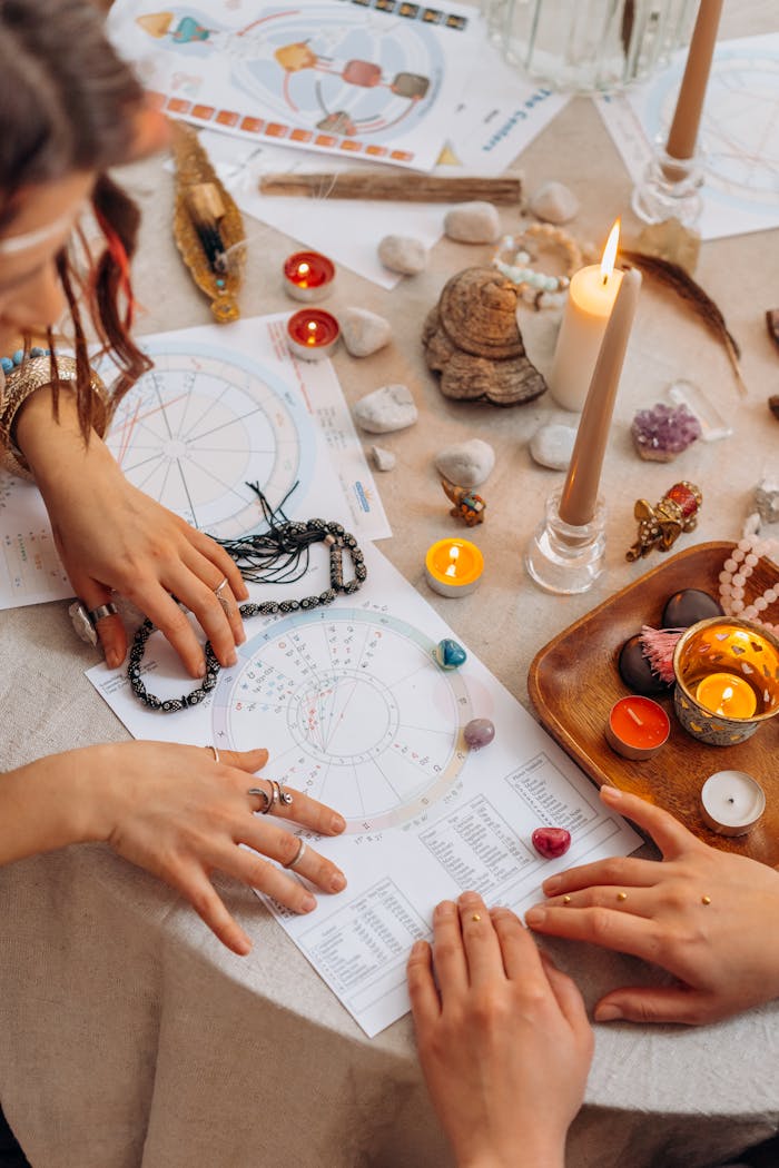 Hands arranging astrology charts with candles and crystals on a table for a spiritual ritual.